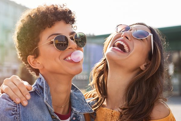 Young,Latin,Woman,Laughing,While,Friend,Inflating,Bubble,Gum.,Closeup